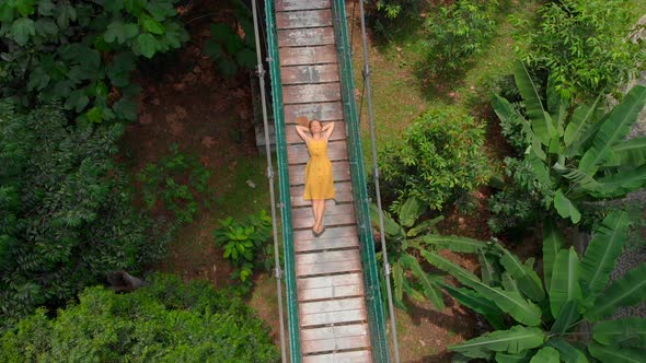 Aerial Shot of a Young Woman Lays on a Suspension Bridge Over the Jungles. Travel To South East Asia