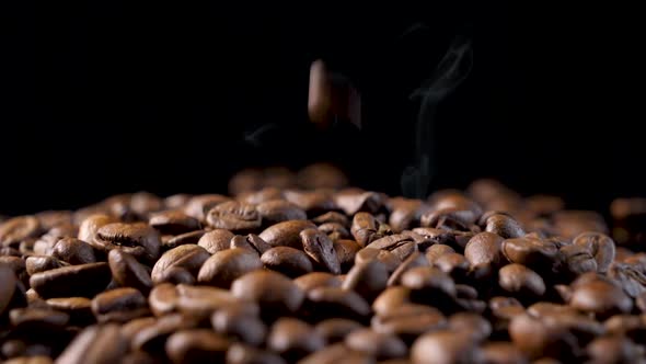 Roasted coffee beans with smoke. Slow motion of arabica coffee seeds falling.