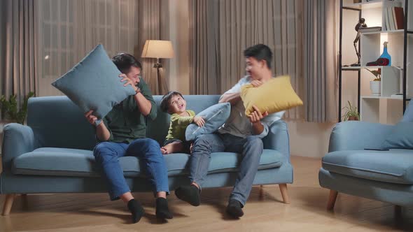 Happy Asian Gay Couple Having Fun With Their Lovely Son Fighting Pillows In Living Room