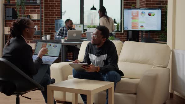 Woman Explaining Data Charts on Laptop and Man Taking Notes