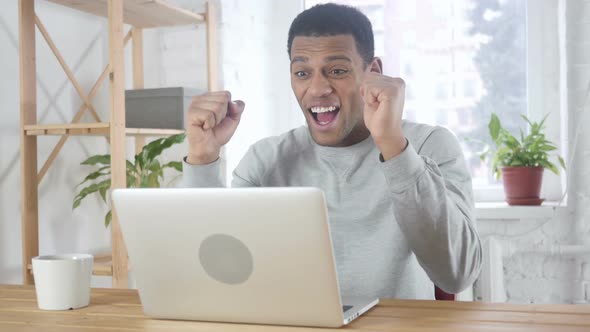 Excited AfroAmerican Man Celebrating Success While Working on Laptop Sitting on Couch