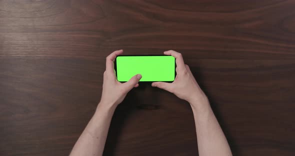 Top View Man Hand Using Smartphone with Green Screen Over Black Walnut Wood Table