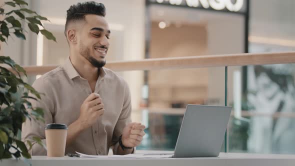 Cheerful Hispanic Man Celebrating Victory Actively Dancing Arab Guy Sitting Looking at Laptop Screen