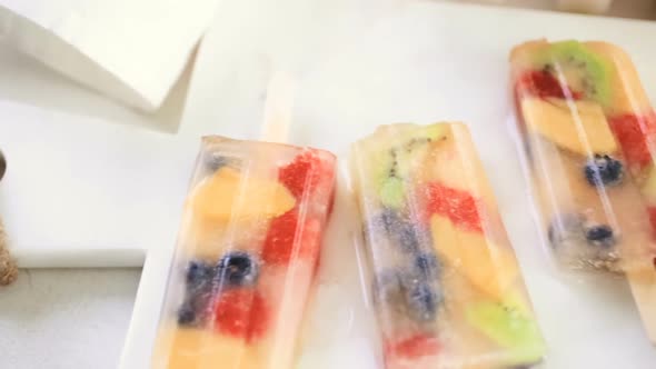 Homemade fresh fruit popsicles with apple juice on marble cutting board with frozen ice pop maker in