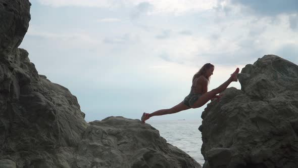 Athletic girl sits in split  in the middle of the sea on the rocks. Flexibility. Yoga. Stretching.