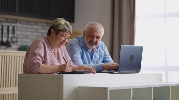 Pair of Retirees are Counting Their Expenses and Income Sitting Together at Kitchen in Apartment Old