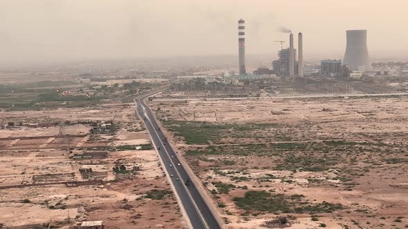 Cinematic color graded aerial shot of silver car driving on country road in desert and big chimneys