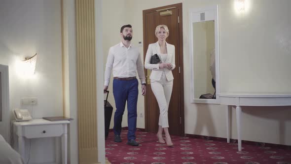 Positive Caucasian Couple with Travel Bag Entering Hotel Room and Talking