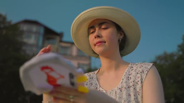 A young beautiful woman in a hat, embroiders a cross on the canvas and smiles at the sunset.