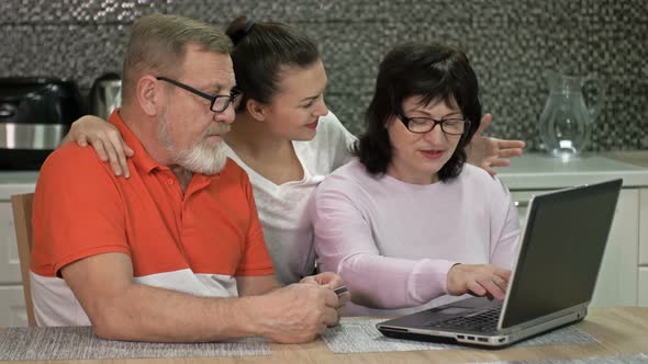 Beautiful Young Woman Is Explaining To Her Elderly Parents How To Shop and Various Payments Online