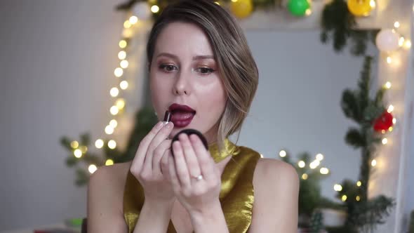 young beautiful woman applying cosmetics near Holiday decorated mirror at home.