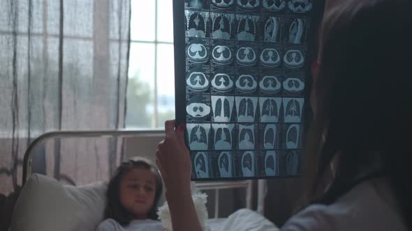 A Doctor Near the Bed of a Sick Girl Looks at MRI X-ray of the Brain