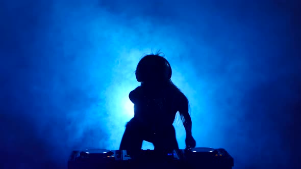 Silhouette of Girl DJ in the Smoke Mixes Music