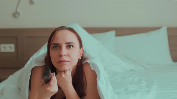 Young Woman Under Blanket Lying on Bed and Watching Tv