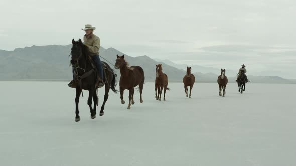 Horses running with cowboys riding across salt flats.