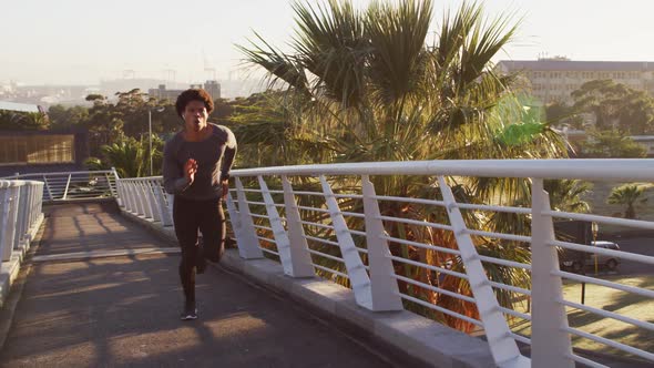 Fit african american man exercising outdoors in city wearing earphones, running on footbridge