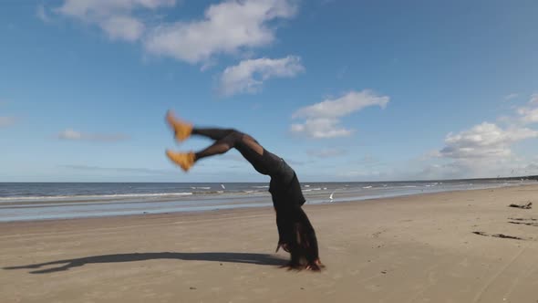 Longhaired Young Woman Practices Front and Back Handspring and Cartwheel on Beach with Sea View