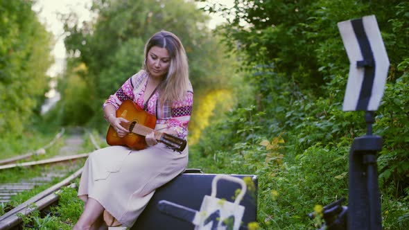 Beautiful Woman Playing on Guitar and Sitting on Suitcase on Railway. Musician Woman Playing Guitar