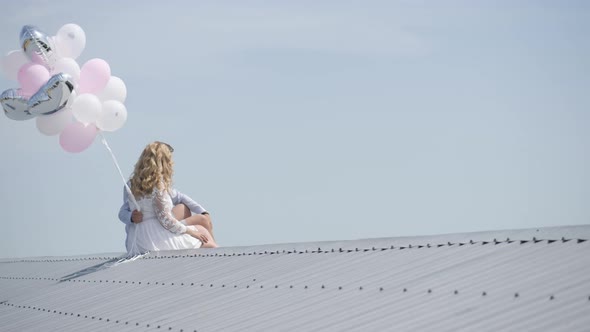 Couple with balloons sitting on a roof