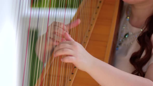 A woman plays a harp in a gazebo in the Park. Hands close up