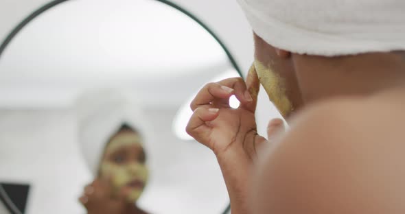 Happy african american woman apply beauty mask on face in bathroom