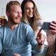 Young Couple in Apartment Looking at Smart Phone and Smiling - VideoHive Item for Sale