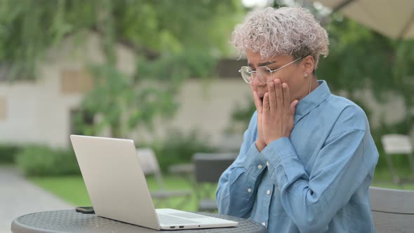 Young African Woman Reacting to Loss on Laptop in Outdoor Cafe