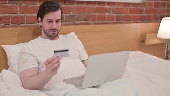 Casual Young Man with Successful Online Payment on Laptop in Bed