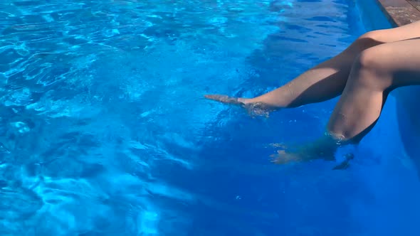 Legs of a Young Woman on the Background of the Blue Water of the Pool