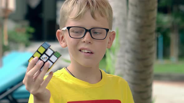 Small Boy in Yellow Tshirt and Glasses Shows Rubik Cube
