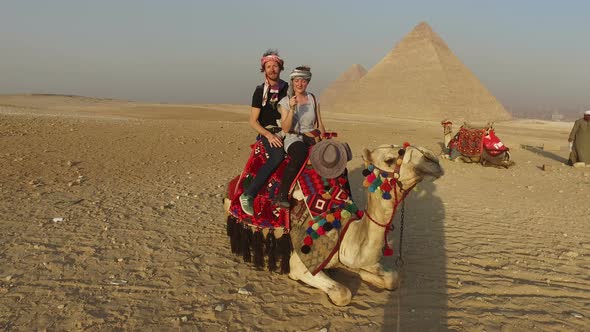 Smiling couple sitting on camel in front of Giza pyramids