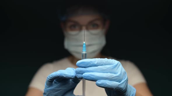 doctor in a mask and gloves raises a syringe with a medicine or vaccine