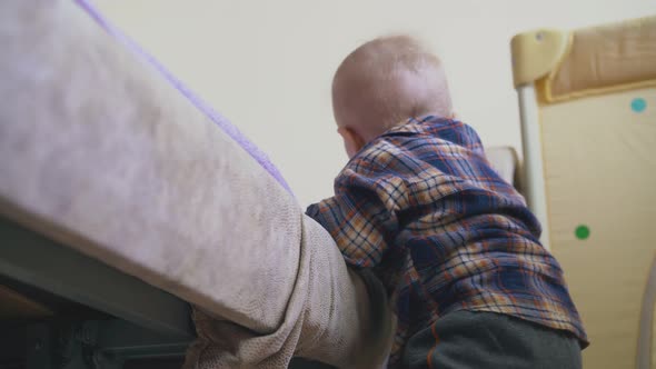 Little Baby in Warm Clothes Climbs on Large Soft Bed in Room