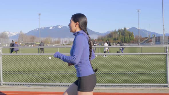 Young Latina woman with braid running on track, Side Follow Shot