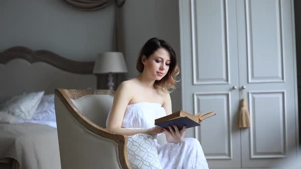 Woman in white dress sitting in armchair in vintage interior and reading a book