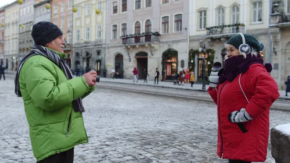 Senior Wife Posing for Camera Laughing While Husband Is Taking Photo Pictures on Winter City Street