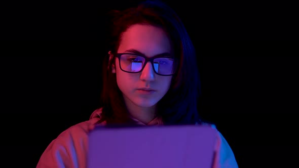 Young Woman with a Tablet. A Woman Is Using a Tablet. Blue and Red Light Falls on a Woman on a Black