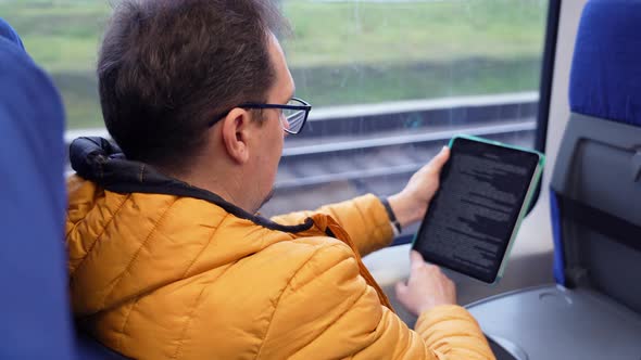 Profile Portrait of Mature Guy in Glasses Reads an Electronic Book While Riding Home By Train