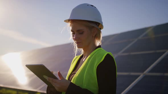 Portrait of a Blonde Female Solar Engineer Standing Uses a Tablet and Looking Away