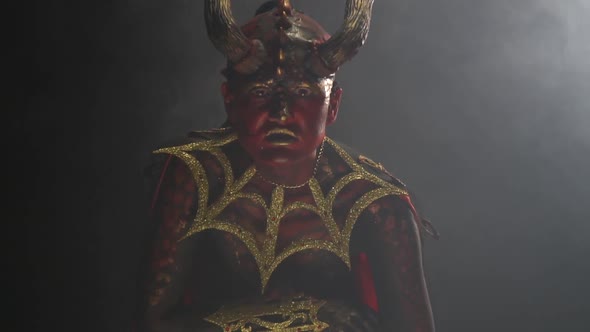 Scary look of a female demon with long horns and red skin, in the smoke