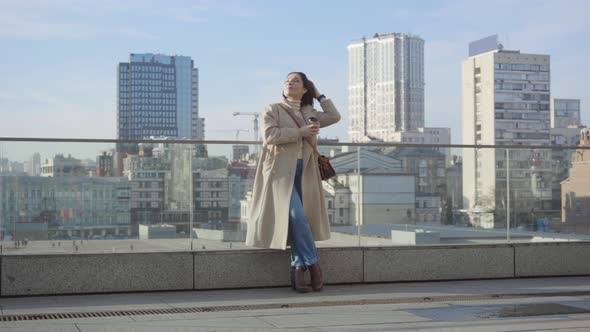 Young Caucasian Businesswoman Standing with Coffee Cup in the City and Looking Away. Confident