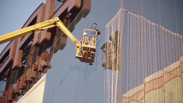 Adult Men with Help of Lifting Crane Hang Garland on Building