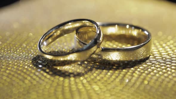Wedding Rings Lying Rotate Spinning on Shiny Golden Shining Surface with Light Closeup Macro