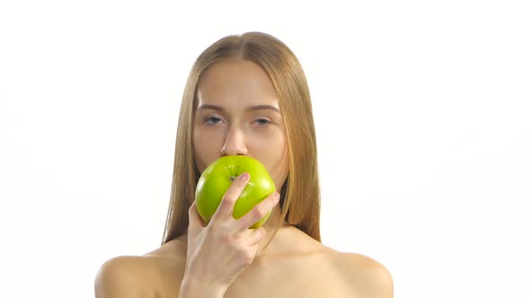 Young Blonde Model Eating a Big Green Apple and Smile. White. Closeup