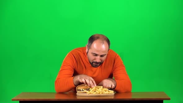 Caucasian Man with Overweight Looks at Delicious Junk Foods on the Table Then Playing with French