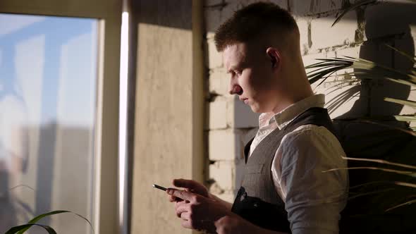 Businessman in His Fashionable Apartments in the Style of Loft. A Young Man Holds a Smartphone and