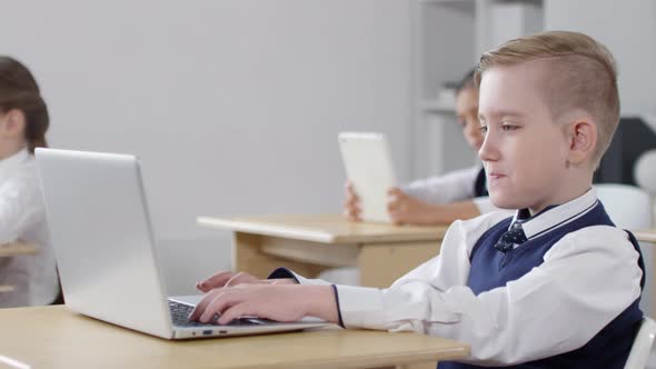 Young Caucasian Schoolboy Watching Tutorial on Laptop in Class