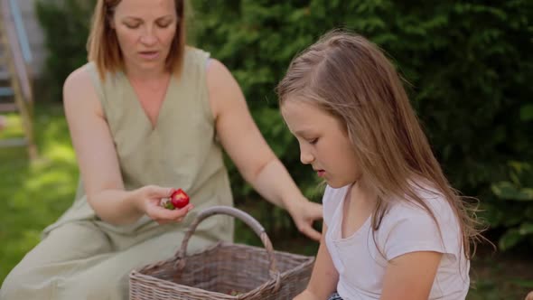 Smiling Mother Feeding Strawberry to Daughter in Backyard