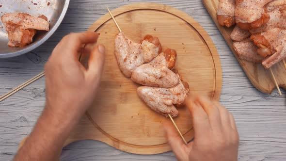 Top View of the Male Hands Piercing Raw Chicken Wings with a Wooden Skewer