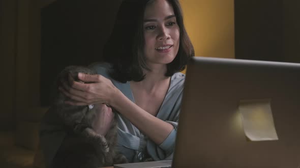 Asian happy business woman work overtime in living room at late night and play with the cat in house